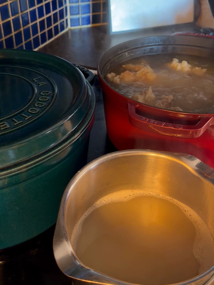 Bone broth gently simmering in red and green pots in our kitchen